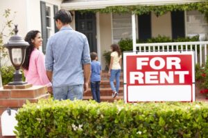 A family looking at a rental property with a large FOR RENT sign in front of the home